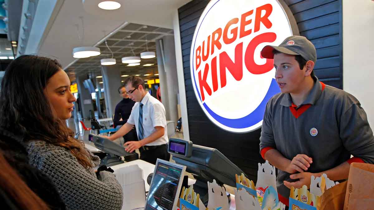 Empleado de Burger King atendiendo a una clienta en el mostrador de un restaurante de comida rápida.