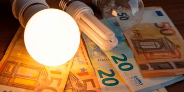 Evolución y subida del precio de la luz en 2025 en Madrid, bombilla iluminada sobre billetes de euro.