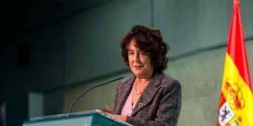 Mujer pronunciando un discurso en un atril con la bandera de España al fondo.