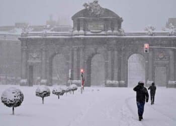 Puerta de Alcalá nevada en Madrid durante la borrasca Konrad, con transeúntes bajo intensas precipitaciones.