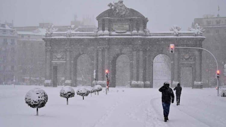 Puerta de Alcalá nevada en Madrid durante la borrasca Konrad, con transeúntes bajo intensas precipitaciones.