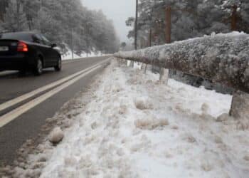 Carretera nevada en Madrid con un coche circulando y barandilla cubierta de hielo.