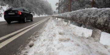 Carretera nevada en Madrid con un coche circulando y barandilla cubierta de hielo.