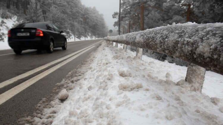 Carretera nevada en Madrid con un coche circulando y barandilla cubierta de hielo.