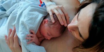 Madre joven sosteniendo a su bebé recién nacido en el hospital, ejemplo de la ayuda a la natalidad de la Comunidad de Madrid de 500 € al mes