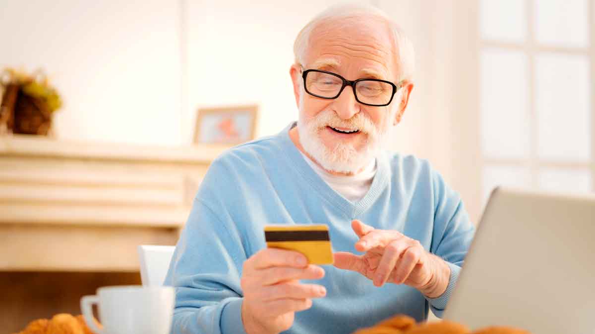 Jubilado usando su ordenador y tarjeta para aprovechar los descuentos del carnet de pensionista