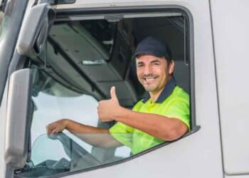 Conductor de camión saludando desde la cabina, ejemplo de profesional del transporte en España