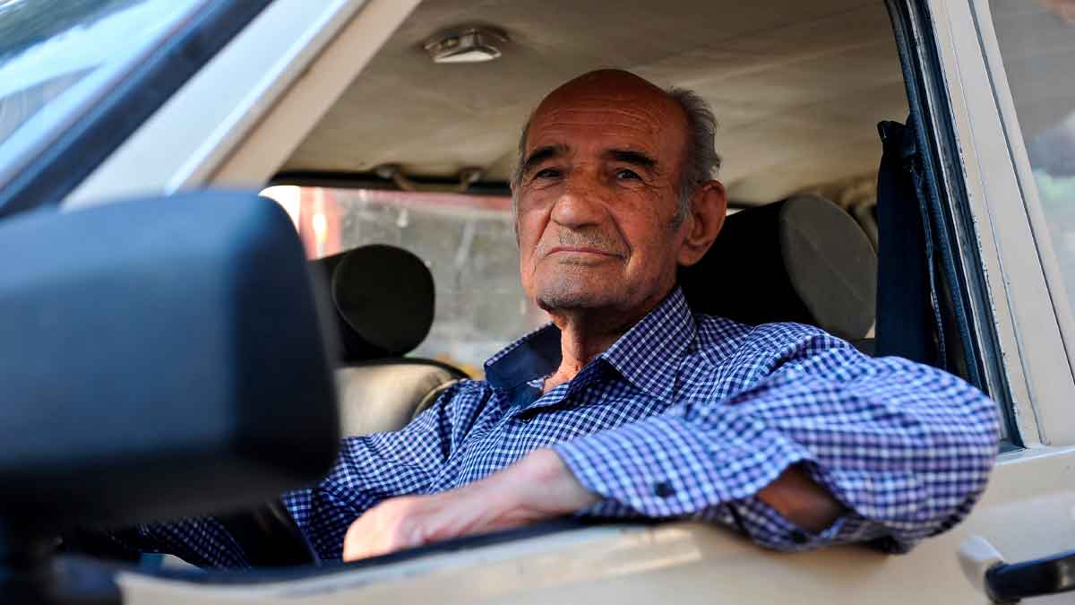 Hombre mayor sentado al volante, afectado por las restricciones de la DGT para enfermedades incapacitantes