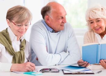 Tres jubilados sonrientes revisan documentos y un libro mientras calculan los impuestos de los que Hacienda les exime