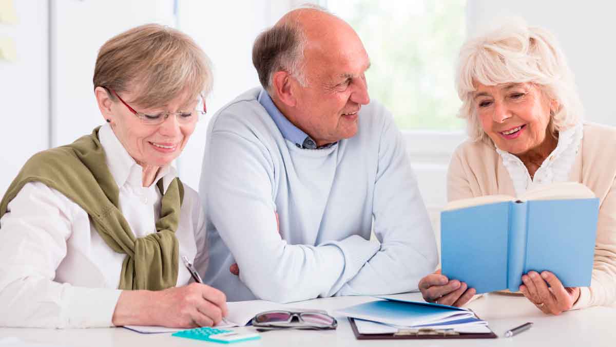 Tres jubilados sonrientes revisan documentos y un libro mientras calculan los impuestos de los que Hacienda les exime