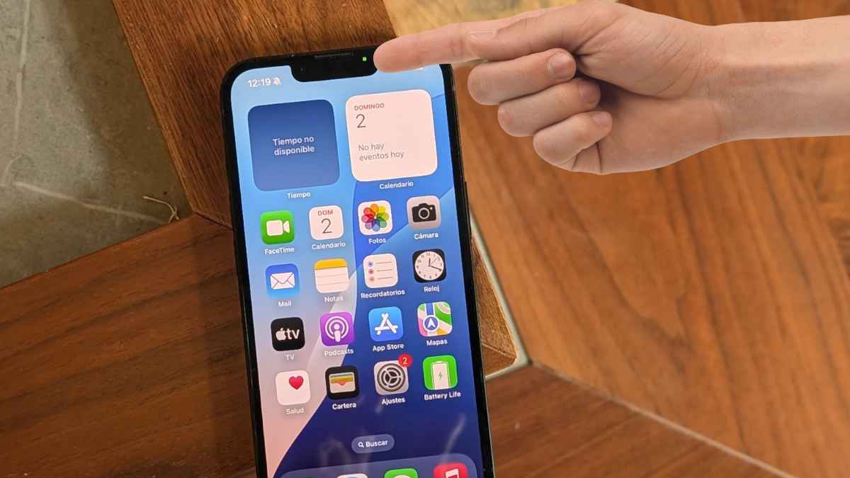 Persona señalando la parte superior de un iPhone, donde se ve el indicador verde o naranja que alerta sobre el uso de cámara o micrófono