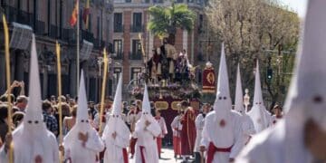 Penitentes con túnicas y capirotes blancos portan un paso de Semana Santa en Madrid ante numerosos fieles