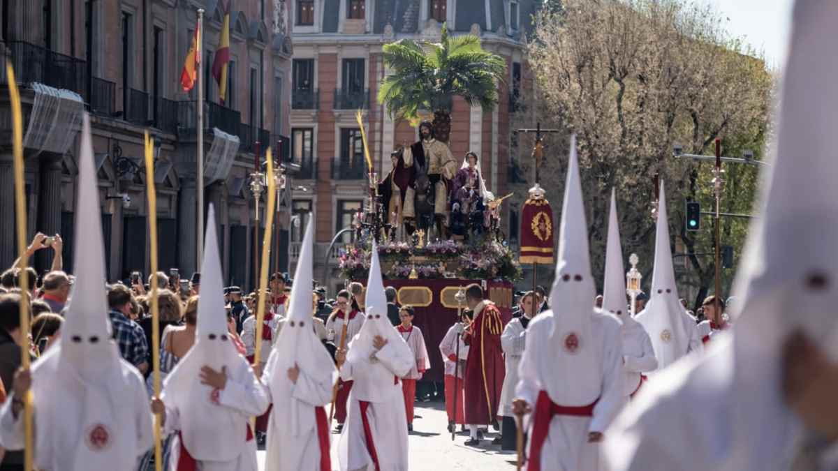 Penitentes con túnicas y capirotes blancos portan un paso de Semana Santa en Madrid ante numerosos fieles