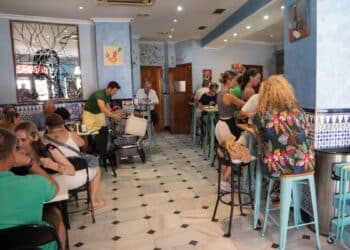 Interior de un bar español con clientes conversando y camareros atendiendo en la barra, reflejando la actividad diaria de la hostelería