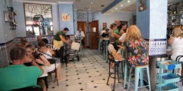 Interior de un bar español con clientes conversando y camareros atendiendo en la barra, reflejando la actividad diaria de la hostelería