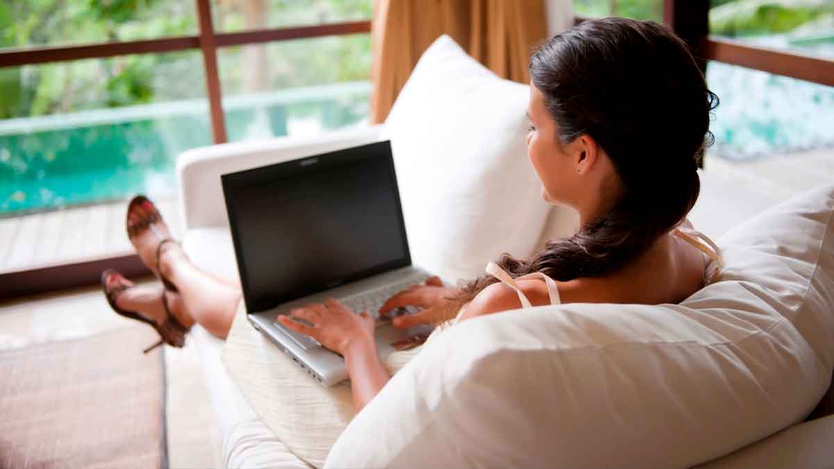 Mujer teletrabajando en casa con portátil, posible accidente laboral