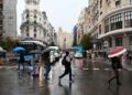 Peatones con paraguas cruzan la Gran Vía de Madrid bajo lluvia intensa, antes de la festividad de San Isidro