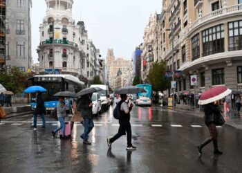 Peatones con paraguas cruzan la Gran Vía de Madrid bajo lluvia intensa, antes de la festividad de San Isidro
