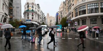 Peatones con paraguas cruzan la Gran Vía de Madrid bajo lluvia intensa, antes de la festividad de San Isidro