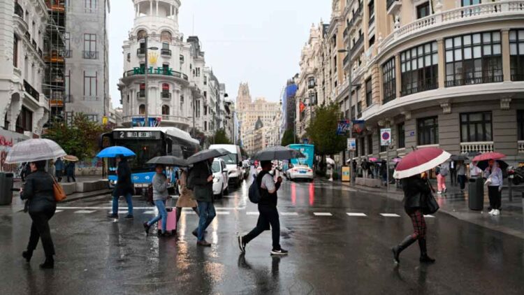 Peatones con paraguas cruzan la Gran Vía de Madrid bajo lluvia intensa, antes de la festividad de San Isidro