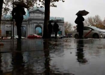 Personas con paraguas frente a la Puerta de Alcalá bajo la lluvia en Madrid, 7 de mayo, según AEMET tiempo inestable