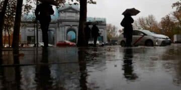 Personas con paraguas frente a la Puerta de Alcalá bajo la lluvia en Madrid, 7 de mayo, según AEMET tiempo inestable