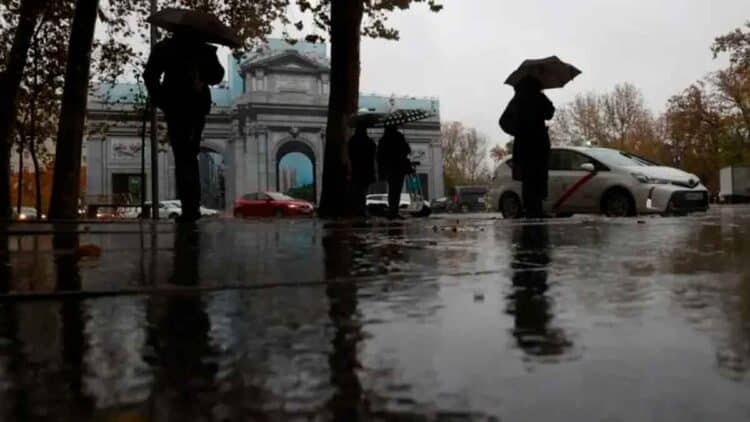 Personas con paraguas frente a la Puerta de Alcalá bajo la lluvia en Madrid, 7 de mayo, según AEMET tiempo inestable