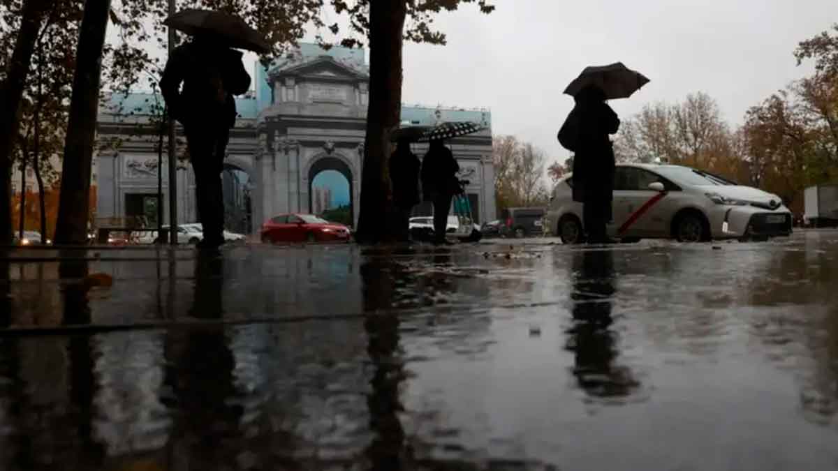 Personas con paraguas frente a la Puerta de Alcalá bajo la lluvia en Madrid, 7 de mayo, según AEMET tiempo inestable