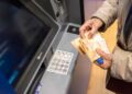 Persona mayor retira efectivo en un cajero automático, sosteniendo billetes de 50 € tras el adelanto de la pensión de mayo 2025