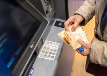 Persona mayor retira efectivo en un cajero automático, sosteniendo billetes de 50 € tras el adelanto de la pensión de mayo 2025