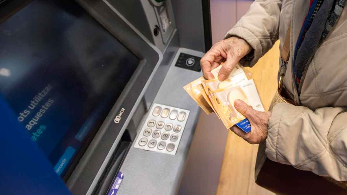 Persona mayor retira efectivo en un cajero automático, sosteniendo billetes de 50 € tras el adelanto de la pensión de mayo 2025