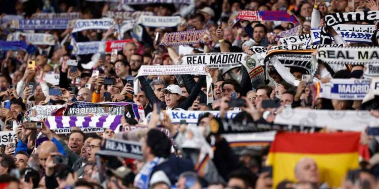 Aficionados del Real Madrid levantan bufandas y móviles en el Santiago Bernabéu, ambiente de grada que disfrutan los socios del club