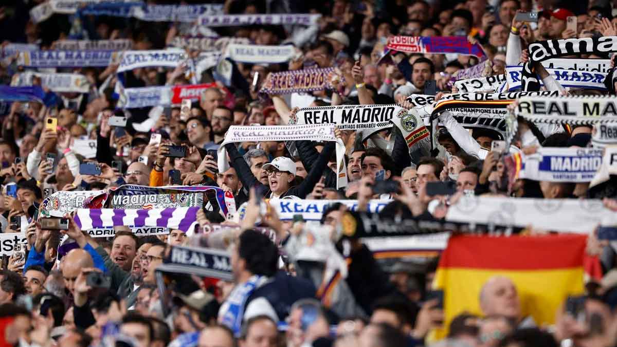 Aficionados del Real Madrid levantan bufandas y móviles en el Santiago Bernabéu, ambiente de grada que disfrutan los socios del club