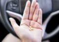 Mano con tres pastillas amarillas frente al volante, símbolo de los medicamentos que pueden impedir renovar el carnet según la DGT
