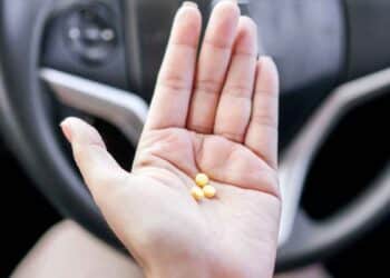 Mano con tres pastillas amarillas frente al volante, símbolo de los medicamentos que pueden impedir renovar el carnet según la DGT