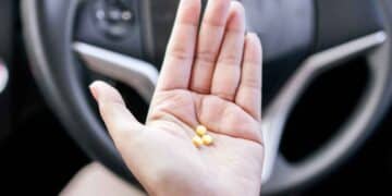 Mano con tres pastillas amarillas frente al volante, símbolo de los medicamentos que pueden impedir renovar el carnet según la DGT