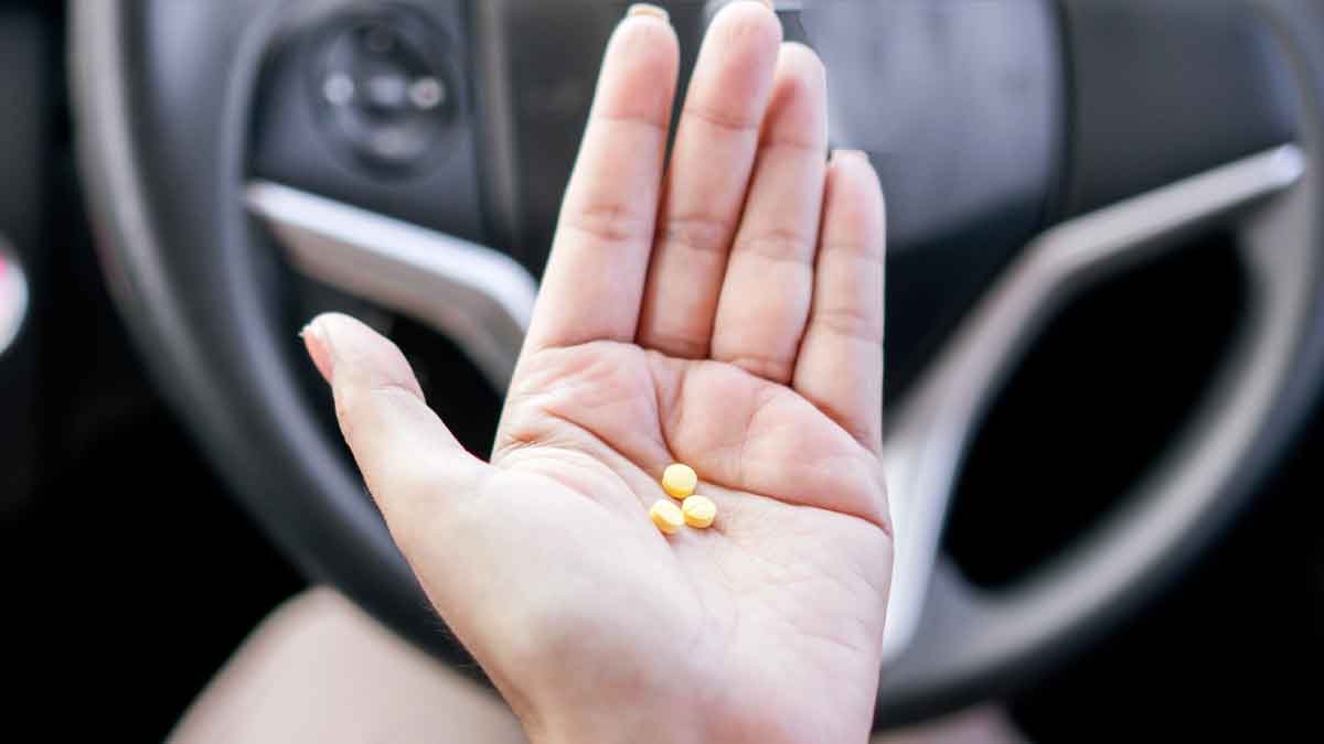 Mano con tres pastillas amarillas frente al volante, símbolo de los medicamentos que pueden impedir renovar el carnet según la DGT