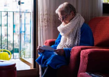 Mujer viuda mayor leyendo carta sobre su pensión de viudedad en el salón de su casa