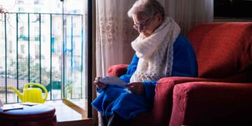 Mujer viuda mayor leyendo carta sobre su pensión de viudedad en el salón de su casa