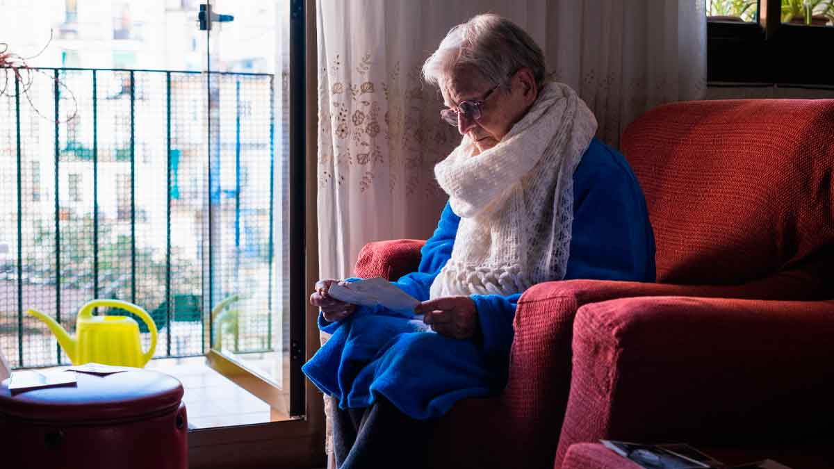 Mujer viuda mayor leyendo carta sobre su pensión de viudedad en el salón de su casa