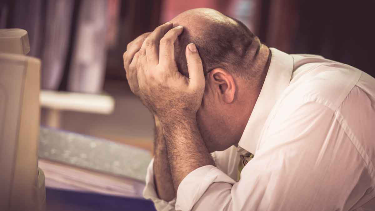 Hombre cabizbajo y preocupado en la oficina, símbolo de las sanciones por contratar a quien cobra paro sin alta en Seguridad Social