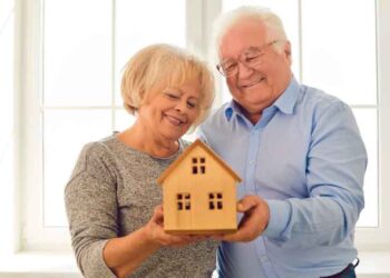 Pareja jubilada mayor de 65 años sosteniendo una maqueta de vivienda en propiedad, ilustrando la advertencia de Hacienda sobre la Declaración de la Renta