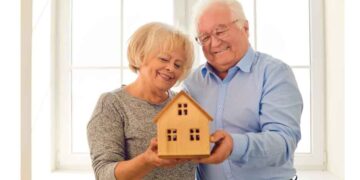 Pareja jubilada mayor de 65 años sosteniendo una maqueta de vivienda en propiedad, ilustrando la advertencia de Hacienda sobre la Declaración de la Renta