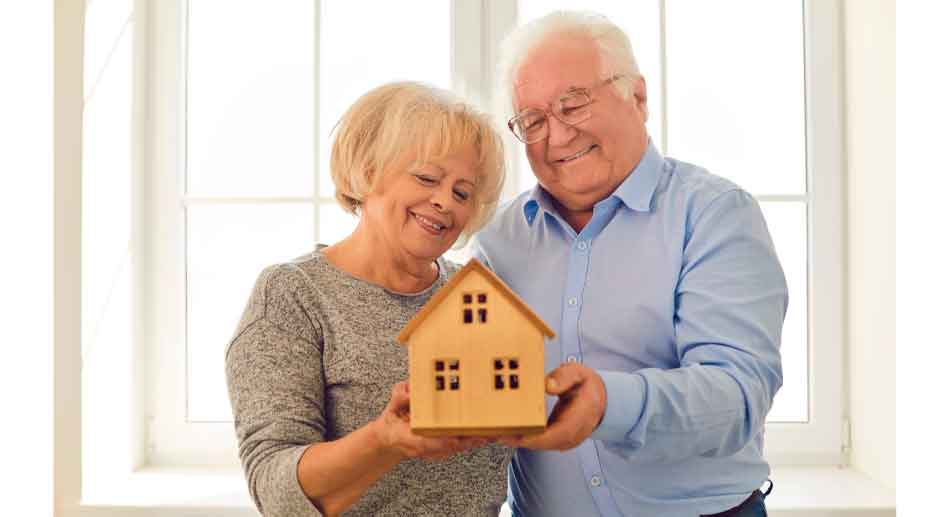 Pareja jubilada mayor de 65 años sosteniendo una maqueta de vivienda en propiedad, ilustrando la advertencia de Hacienda sobre la Declaración de la Renta