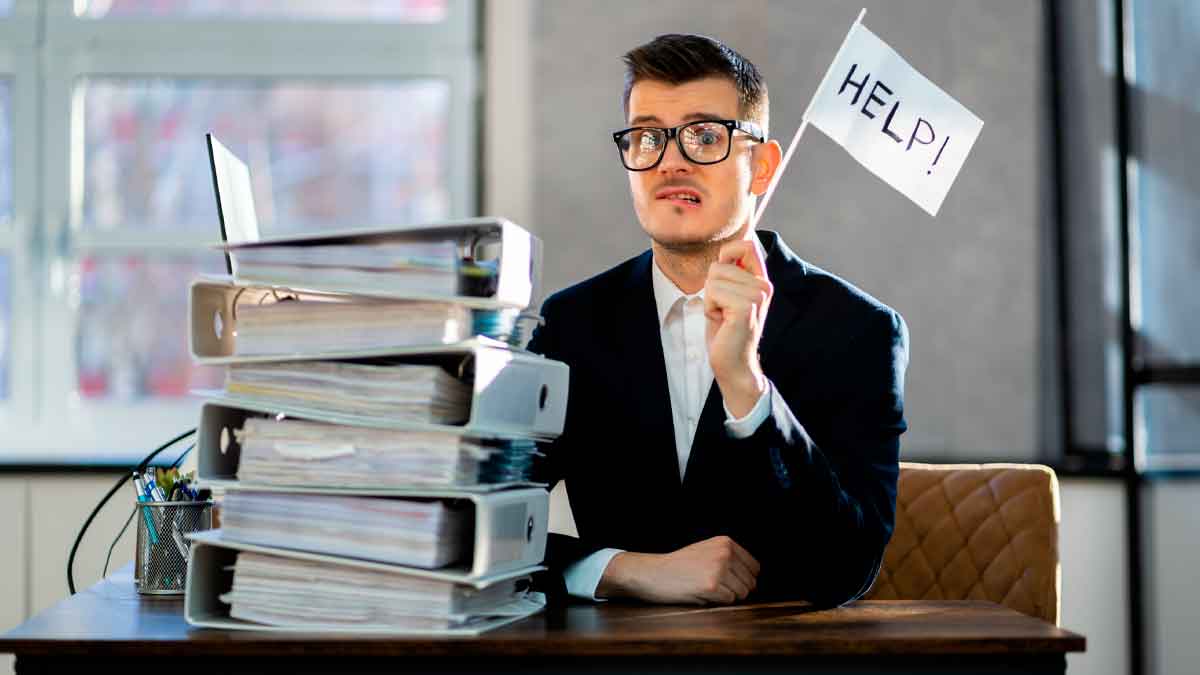 Hombre con gafas rodeado de archivadores alza una bandera de “HELP”, símbolo de la obligación de guardar facturas para Hacienda