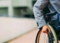 Persona en silla de ruedas con chaqueta gris empujando la rueda, ilustración de las ayudas por discapacidad del 50 % en 2025
