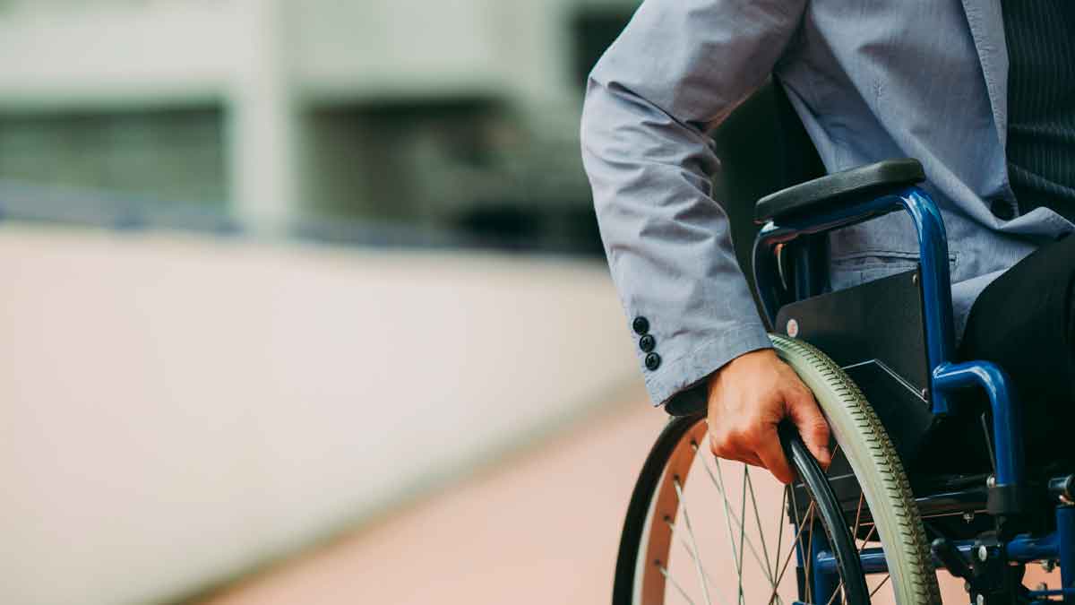 Persona en silla de ruedas con chaqueta gris empujando la rueda, ilustración de las ayudas por discapacidad del 50 % en 2025