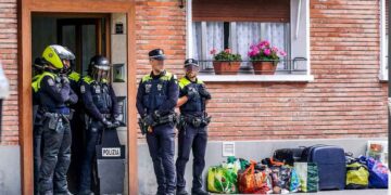 Policías municipales vigilan la entrada de una vivienda social con maletas y bolsas en la acera durante un desahucio por ocupación ilegal en Madrid