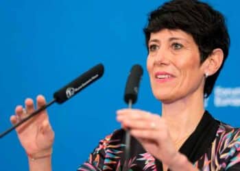 Elma Saiz explica la compatibilidad entre paro y jubilación durante una rueda de prensa, con micrófonos y fondo azul