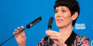 Elma Saiz explica la compatibilidad entre paro y jubilación durante una rueda de prensa, con micrófonos y fondo azul